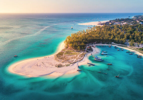 Aerial view of the fishing boats on tropical sea coast with sandy beach at sunset. Summer holiday on Indian Ocean, Zanzibar, Africa. Landscape with boat, green trees, transparent blue water. Top view